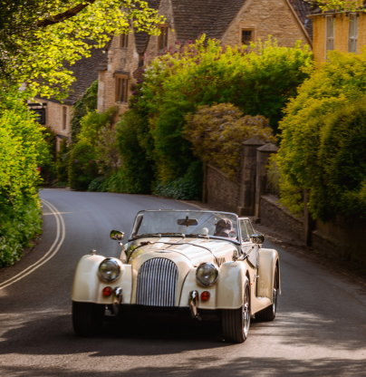 A classic car driving on a Cotswold country road